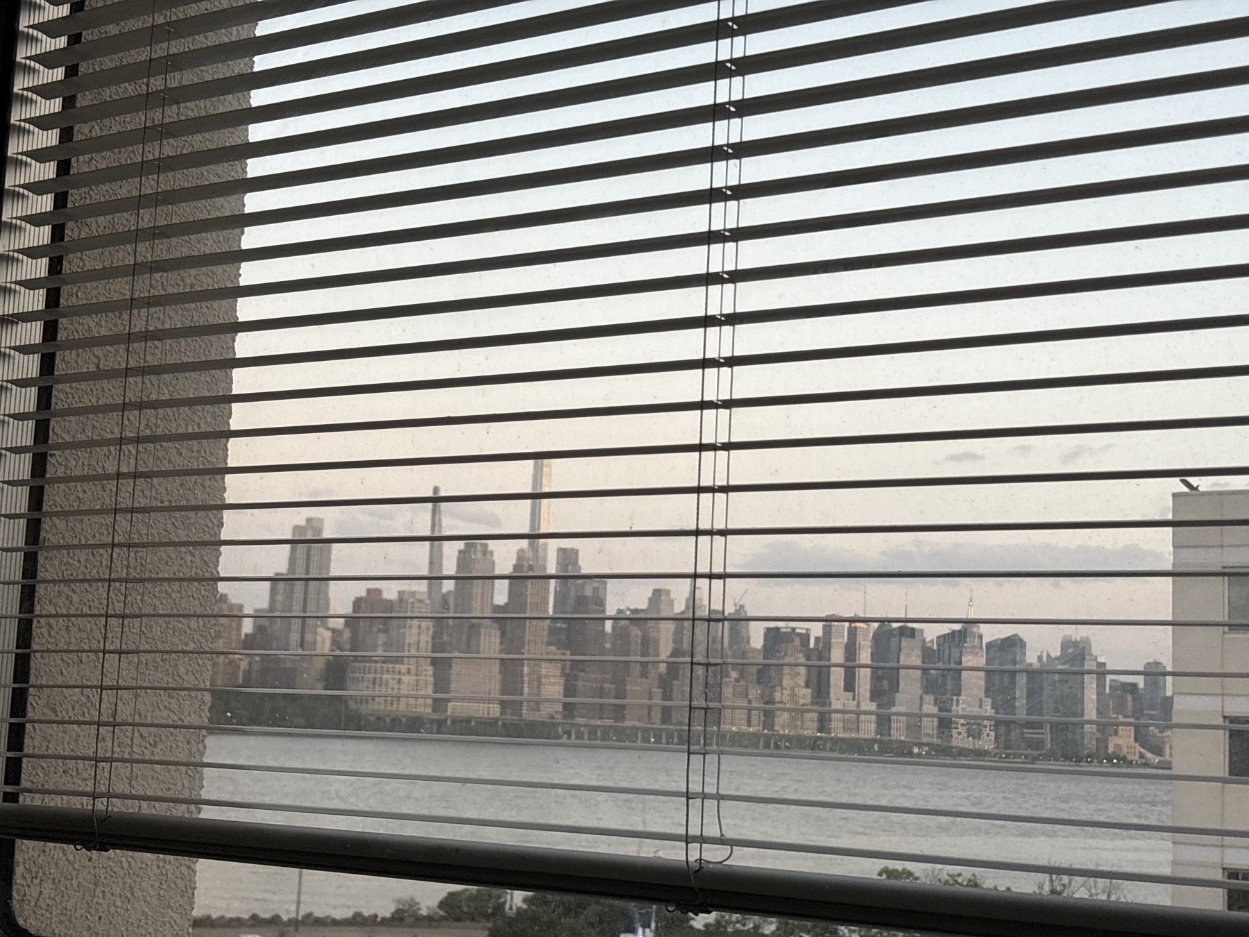 A view of the New York City skyline from across the river through window blinds.