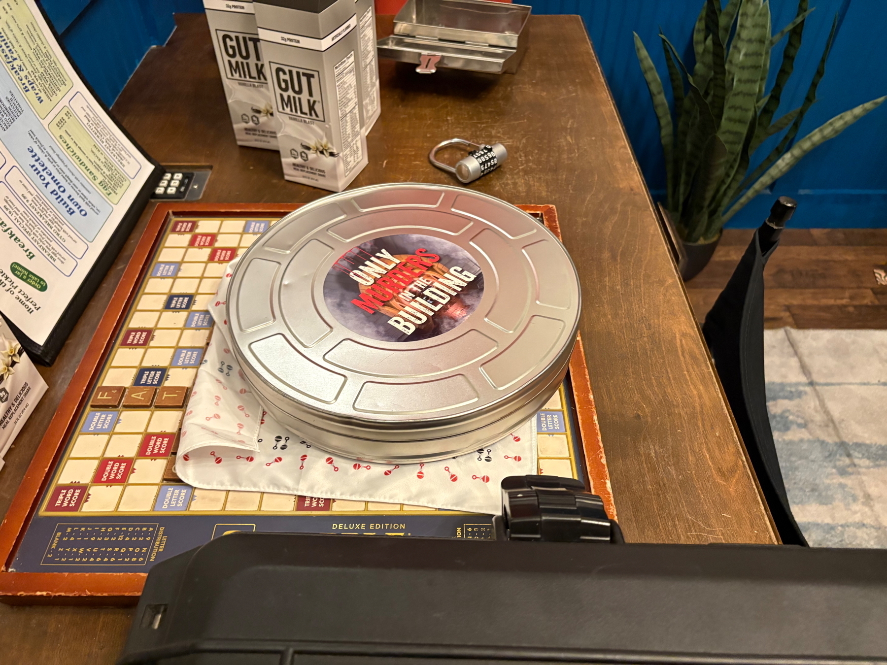 A film canister with the logo for “Only Murders in the Building” sits atop a Scrabble board on a desk.